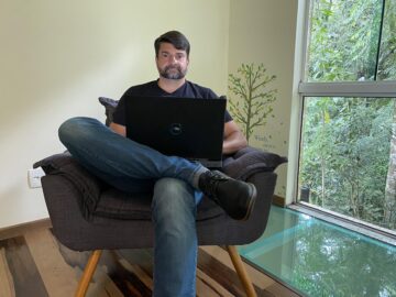 CEO do portal cessão de créditos, maxiuel cerzida sentado em uma poltrona com as pernas cruzadas e um laptop em seu colo